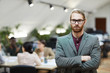 © Seventyfour - Waist up portrait of bearded businessman wearing glasses posing in office standing with arms crossed and looking at camera, copy space