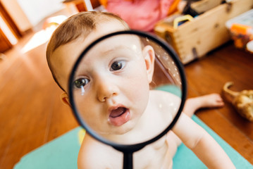 Wall Mural - Baby face while playing with a magnifying glass, which makes a funny and tender face.