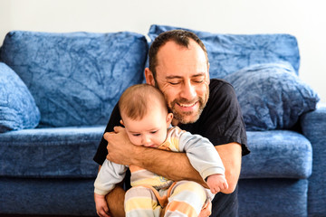 Wall Mural - Father sitting on the floor with his baby in his arms in the living room of home.