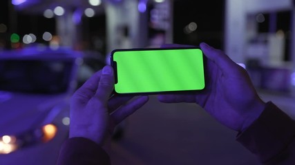 Colorful blue light man hands holding use smartphone with horizontal green screen on night city background white car communication device hands digital gadget phone touchscreen mobile slow motion