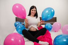 Beautiful Young Pregnant Girl Sitting On Bed Holding Pink And Blue Balloons , Boy Or A Girl .