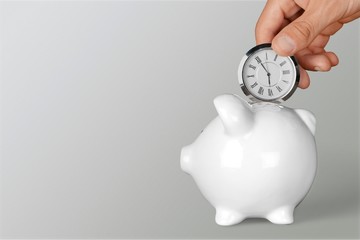 Hand depositing  clock  in piggy bank on background