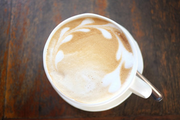 Latte coffee in the white cup on wooden foods table.