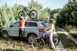 © rh2010 - Young couple preparing for the bicycle riding, picking up mountain bicycle from the car trunk during the summer vacations in the forest