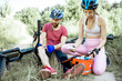 © rh2010 - Woman giving first aid to a man with knee injury while cycling on the mountain bicycles on the forest road during the summer time