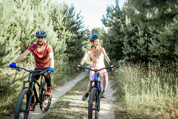 Young man and woman riding mountain bicycles on the forest road during the summer time