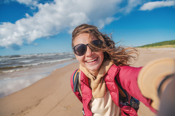 Young happy beautiful girl making selfie on a beautiful cold Baltic beach, traveling to northern Europe