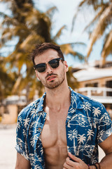 Handsome mature male model enjoying a sunny day on the beautiful island of Boracay. Walking with open blue shirt between palm trees on famous white beach.