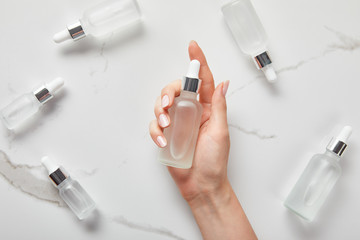 Wall Mural - cropped view of woman hand with moisturizer serum near cosmetic glass bottles on white surface