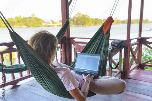 Cuadros en Lienzo Woman working with laptop on hammock hanging in tourist resort on the Mekong River, Laos