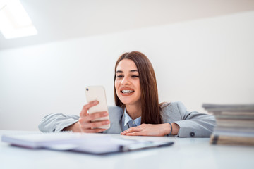 Wall Mural - Beautiful businesswoman in formalwear using smart phone while sitting at desk with paper documents.