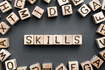 Fototapete - the word skills wooden cubes with burnt letters, skill acquisition, gray background top view, scattered cubes around random letters
