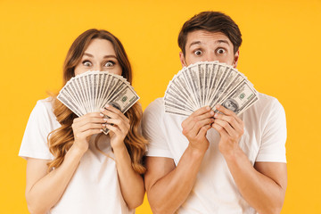 Portrait of happy couple man and woman in basic t-shirts rejoicing while holding bunch of dollar money