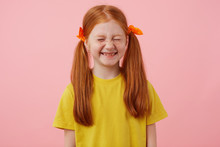 Portrait Of Little Freckles Red-haired Girl With Two Tails, Smiles With Closed Eyes, Wears In Yellow T-shirt, Stands Over Pink Background.