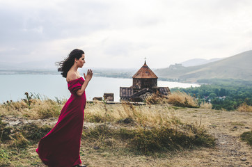 Wall Mural - Portrait of young woman in red dress standing near monastery and pray, Armenia