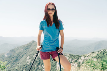 Wall Mural - Beautiful sporty woman walking with trekking poles high in summer mountains.