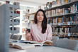 © standret - Looking forward. Brunette girl in casual clothes having good time in the library full of books