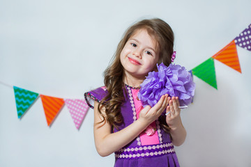 Wall Mural - Little girl holding a paper pompon on a white background and colored garlands. Theme holiday, birthday.