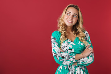 Poster - Cheerful happy cute young blonde girl in bright blue dress posing isolated over red wall background looking aside.