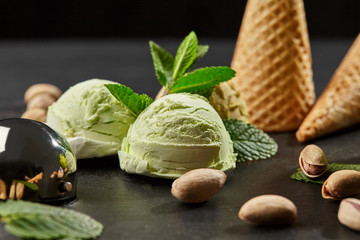 Wall Mural - Tasty pistachio ice cream decorated with fresh mint and served on a stone slate over a black background.