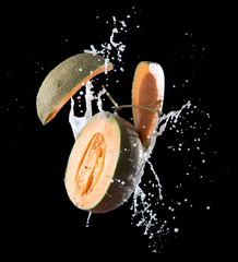 Poster - Fresh melon with milk splash flying in the air isolated on black