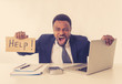 © SB Arts Media - Depressed sad and frustrated young businessman holding a help sign in stress at workplace
