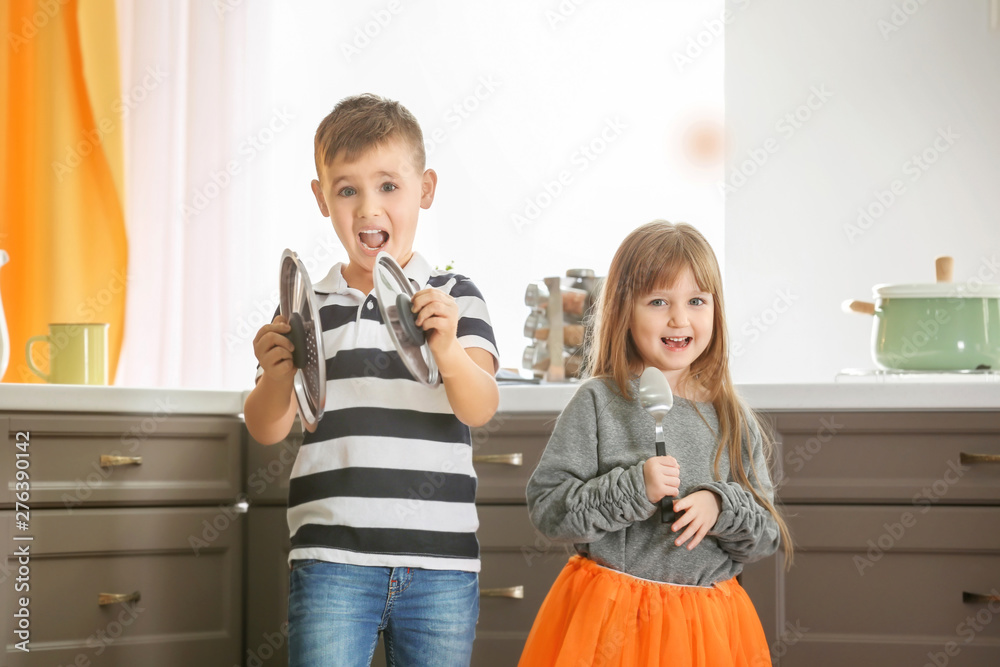 Cute little children playing as musical band in kitchen