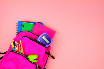 Wall Mural - Pink backpack full of school supplies against a pink paper background. Top view with copy space.