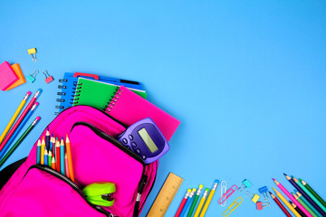 Wall Mural - Pink backpack with corner border of school supplies against a blue paper background. Top view with copy space.
