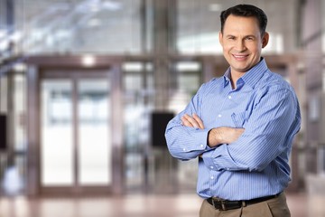 Portrait of handsome middle aged businessman standing with arms crossed on modern city building background