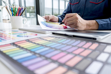 Poster - Male creative graphic designer working on color selection and color swatches, drawing on graphics tablet at workplace with work tools and accessories