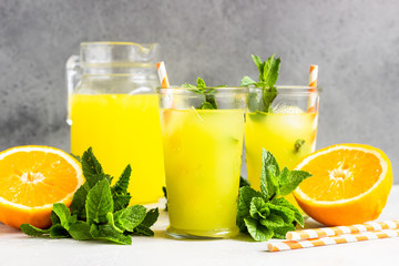 Orange lemonade in glass with fresh orange and mint over light grey stone table. Refreshing summer drink. Cocktail bar background concept. Copy space.