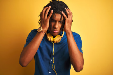 Afro american man with dreadlocks wearing headphones over isolated yellow background suffering from headache desperate and stressed because pain and migraine. Hands on head.