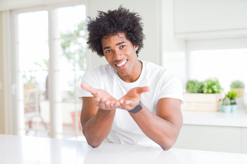 Sticker - Young african american man wearing casual white t-shirt sitting at home Smiling with hands palms together receiving or giving gesture. Hold and protection