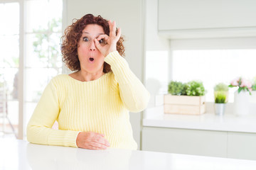 Poster - Beautiful senior woman wearing yellow sweater doing ok gesture shocked with surprised face, eye looking through fingers. Unbelieving expression.