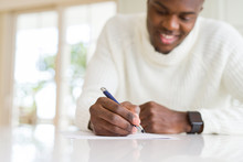 Close Up Of African Man Writing A Note On A Paper Smiling Confident