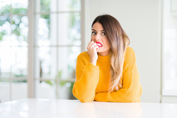 Canvas Print - Young beautiful woman wearing winter sweater at home looking stressed and nervous with hands on mouth biting nails. Anxiety problem.