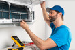 Installation service fix  repair maintenance of an air conditioner indoor unit, by cryogenist technican worker checking the air filter in blue shirt baseball cap
