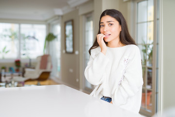 Poster - Young beautiful woman at home on white table looking stressed and nervous with hands on mouth biting nails. Anxiety problem.