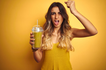 Poster - young beautiful woman drinking detox green smoothy over yellow isolated background annoyed and frust