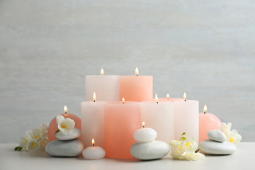 Beautiful composition with candles, stones and flowers on table against light background