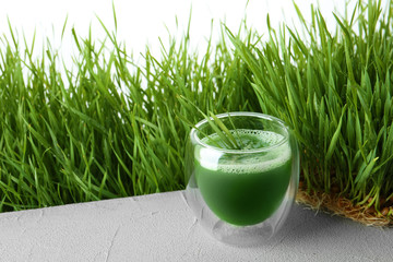 Glass of juice and fresh wheat grass on background. Space for text