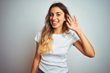 Sticker - Young beautiful woman wearing casual white t-shirt over isolated background smiling with hand over ear listening an hearing to rumor or gossip. Deafness concept.