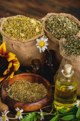 Wall Mural - sackcloth bags with dried herbs, bottles with essential oils and chamomile flowers on wooden surface