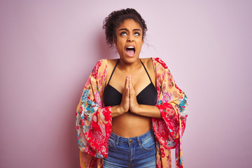 Sticker - American woman on holiday wearing bikini and colorful dress over isolated pink background begging and praying with hands together with hope expression on face very emotional and worried.