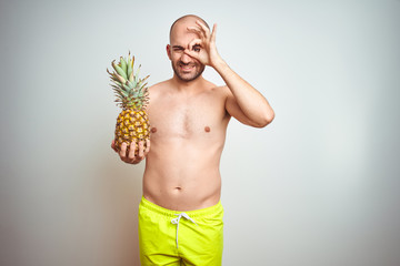 Sticker - Young man wearing summer hat and swimwear holding pineapple over isoalted background with happy face smiling doing ok sign with hand on eye looking through fingers