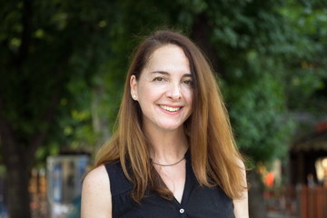 Portrait of a mature woman, 40s, smiling looking camera outdoors in a city.