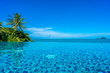 Beautiful luxury outdoor swimming pool in hotel resort with sea ocean around coconut palm tree and white cloud on blue sky