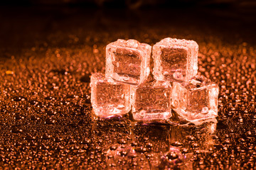 Ice cubes in red light on black wet table.