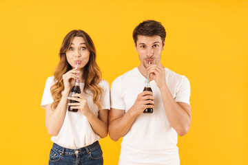 Portrait of beautiful couple man and woman in basic t-shirts standing together while drinking soda beverage with straws